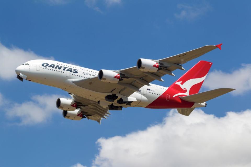 A Qantas plane flies through the clouds on a sunny day.