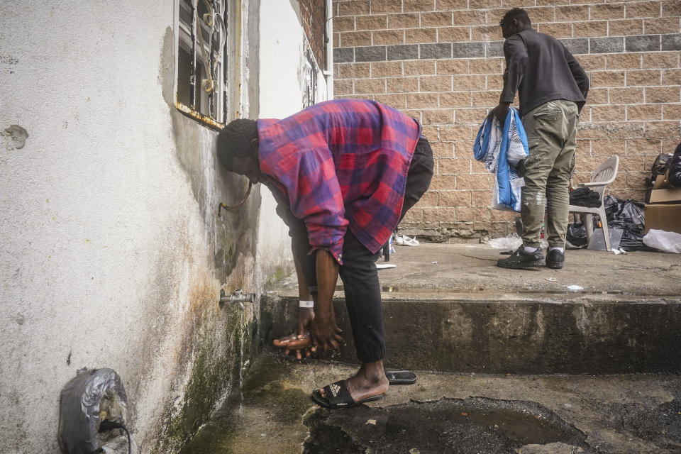 A Senegalese migrant, left, washes his feet at a pipe in the backyard at Bronx's Masjid Ansaru-Deen mosque, Friday March 15, 2024, in New York. The mosque, formerly the family home for its Imam Omar Niass, has served as a temporary shelter and refuge since 2020 for hundreds of African migrants, while seeking asylum in the United States. (AP Photo/Bebeto Matthews)