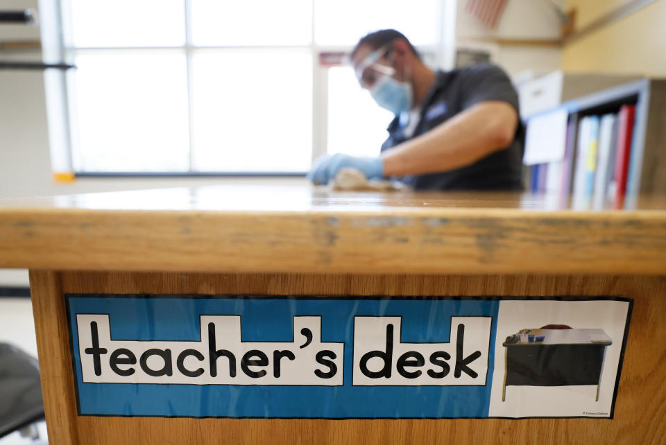 Des Moines Public Schools custodian Joel Cruz cleans a teacher's desk in a classroom at Brubaker Elementary School, Wednesday, July 8, 2020, in Des Moines, Iowa. School districts that plan to reopen classrooms in the fall are wrestling with whether to require teachers and students to wear face masks. In Iowa, among other places, where Democratic-leaning cities like Des Moines and Iowa City have required masks to curb the spread of the coronavirus, while smaller, more conservative communities have left the decision to parents. (AP Photo/Charlie Neibergall)