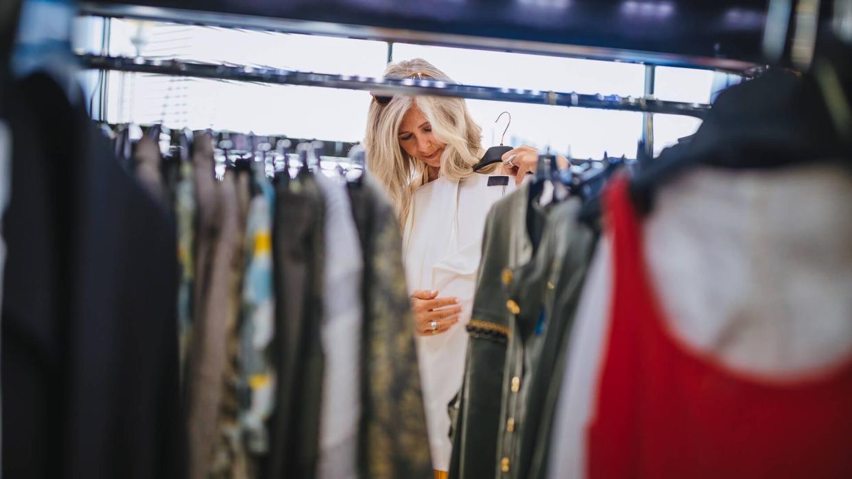 Fashionable senior woman with gray hair looking for clothes and choosing in urban clothes store.