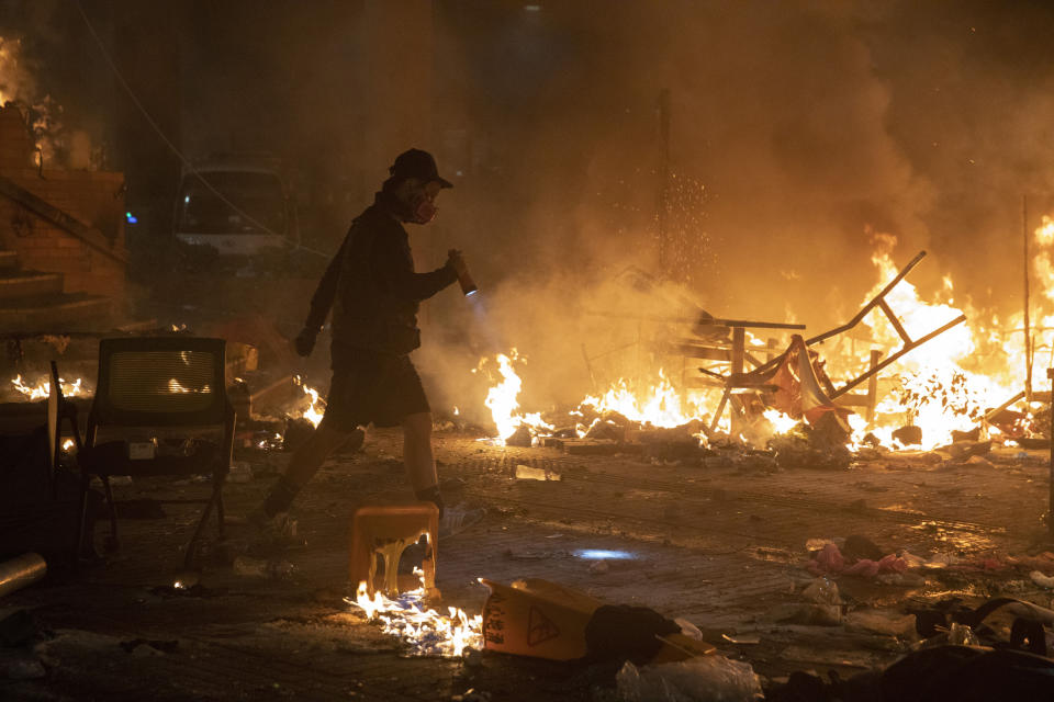 A protester walks past burning debris as police storm part of the Hong Kong Polytechnic University campus during the early morning hours in Hong Kong, Monday, Nov. 18, 2019. Police breached the university campus held by protesters early Monday after an all-night siege that included firing repeated barrages of tear gas and water cannons. (AP Photo/Ng Han Guan)