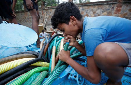 A boy uses his mouth to pump water out from a municipal tanker to fill his containers in New Delhi, India, June 26, 2018. REUTERS/Adnan Abidi