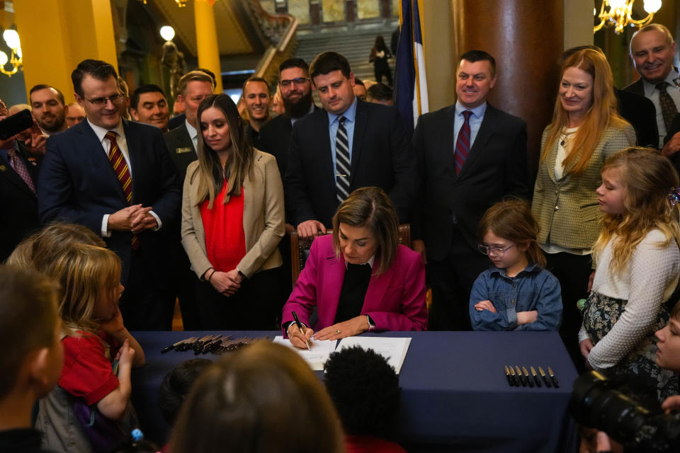 Gov. Kim Reynolds signs House File 68, her private school scholarships bill, as kids from private schools look on, in the rotunda of the Iowa Capitol on Tuesday, Jan. 24, 2023.