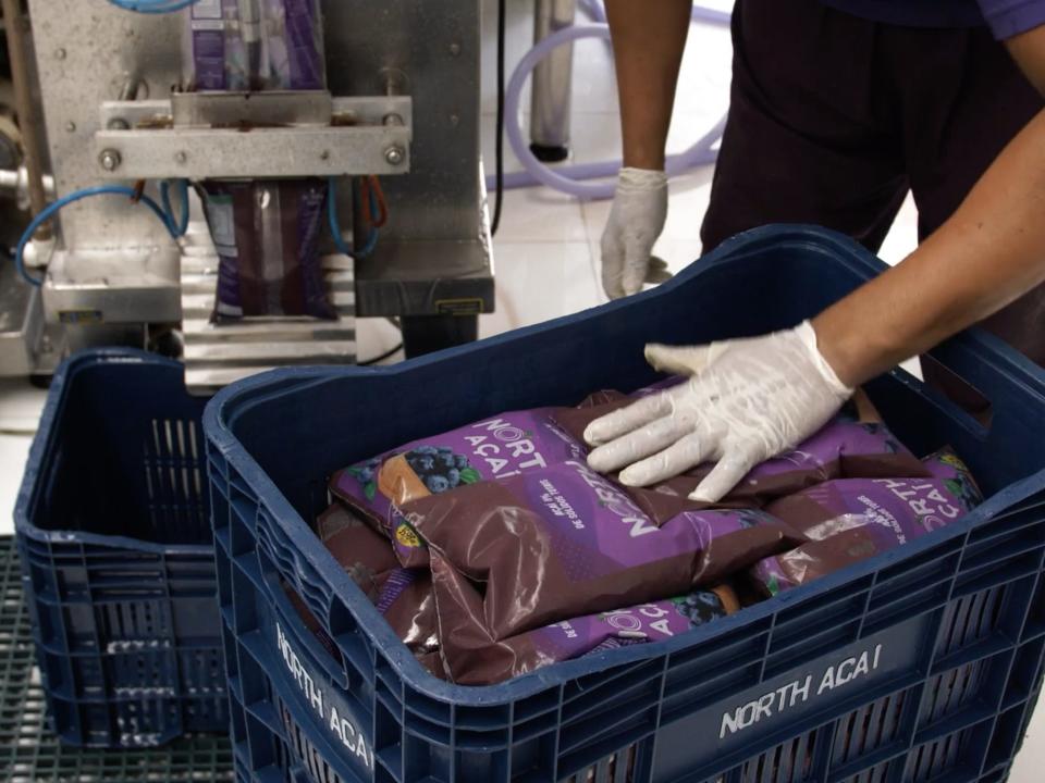 A hand stacks bags of processed açaí in a basket.