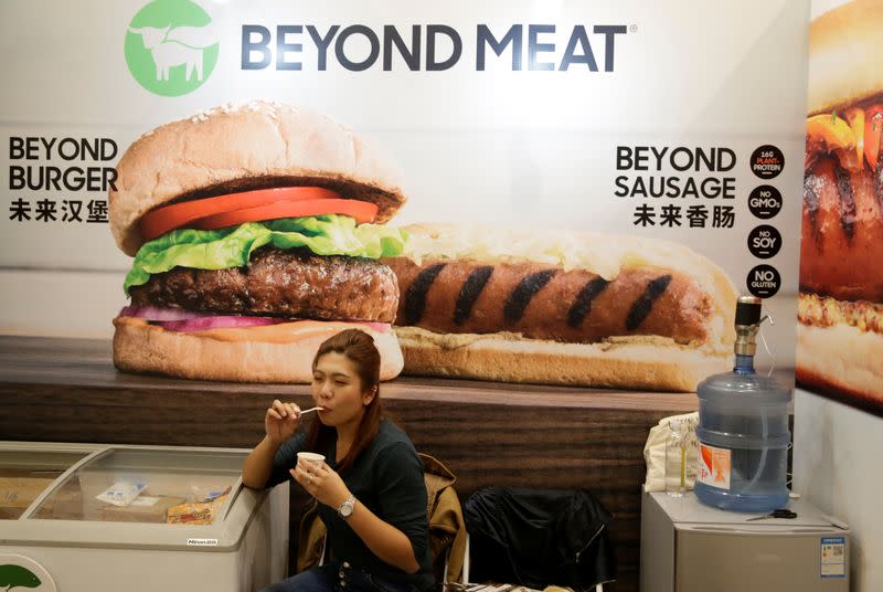 A woman sits next to a poster at the booth of plant-based food company Beyond Meat at VeggieWorld fair in Beijing