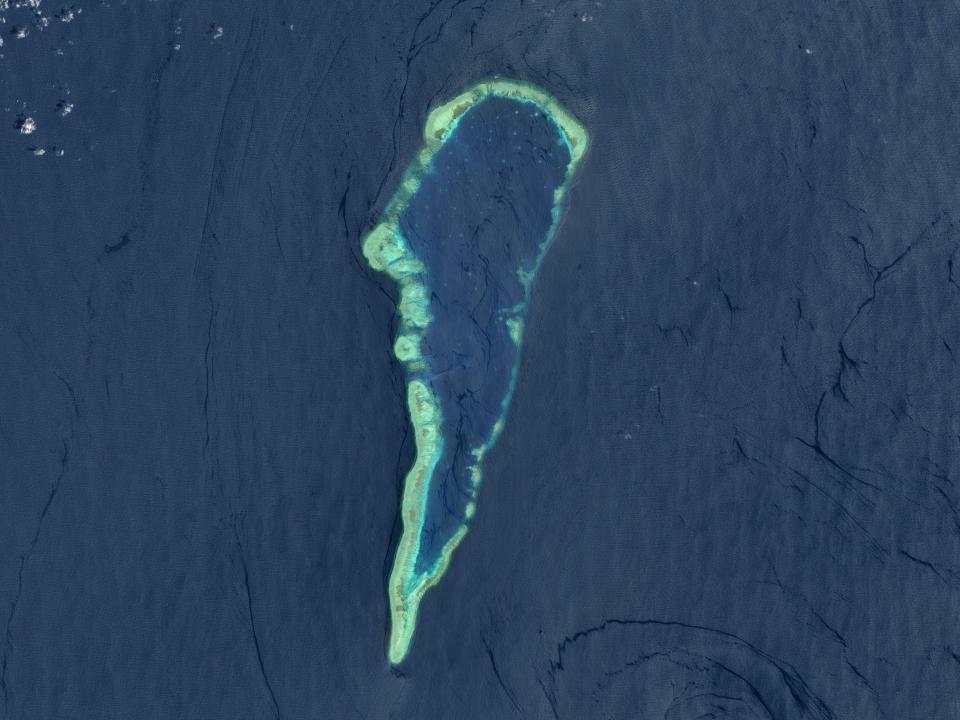 An aerial view of the Second Thomas Shoal in the South China Sea. It looks like a ring of light green in a sea of blue with a larger collection of deep blue ocean water inside the ring of light green.