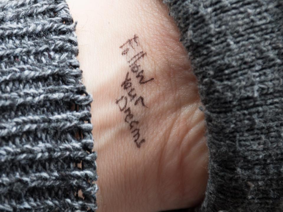 Handwritten "follow your dreams" tattoo on person's wrist