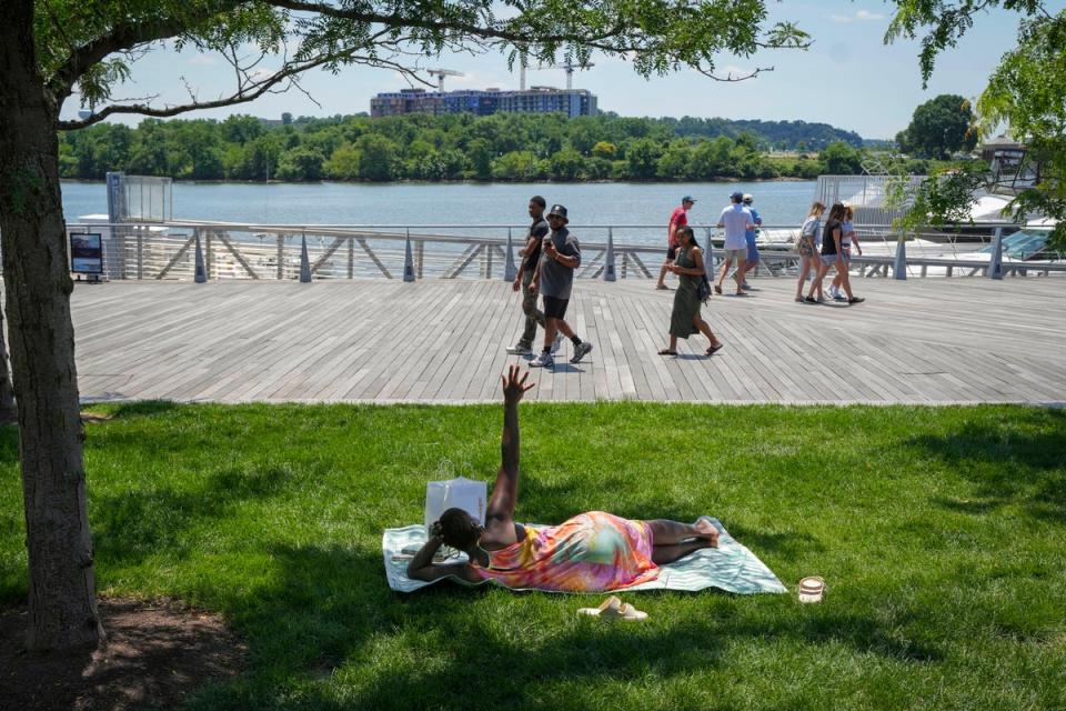 Forecasters say more than 135 million Americans will face temperatures above 90 degrees for most of the week. A woman stretches up her hand while lying in a patch of shade with a book at Yards Park near Washington, DC (AP)