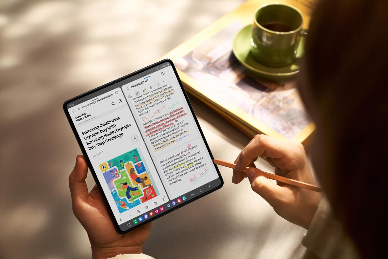A person makes notes on the Galaxy Z Fold 5 phone using a stylus while drinking coffee.
