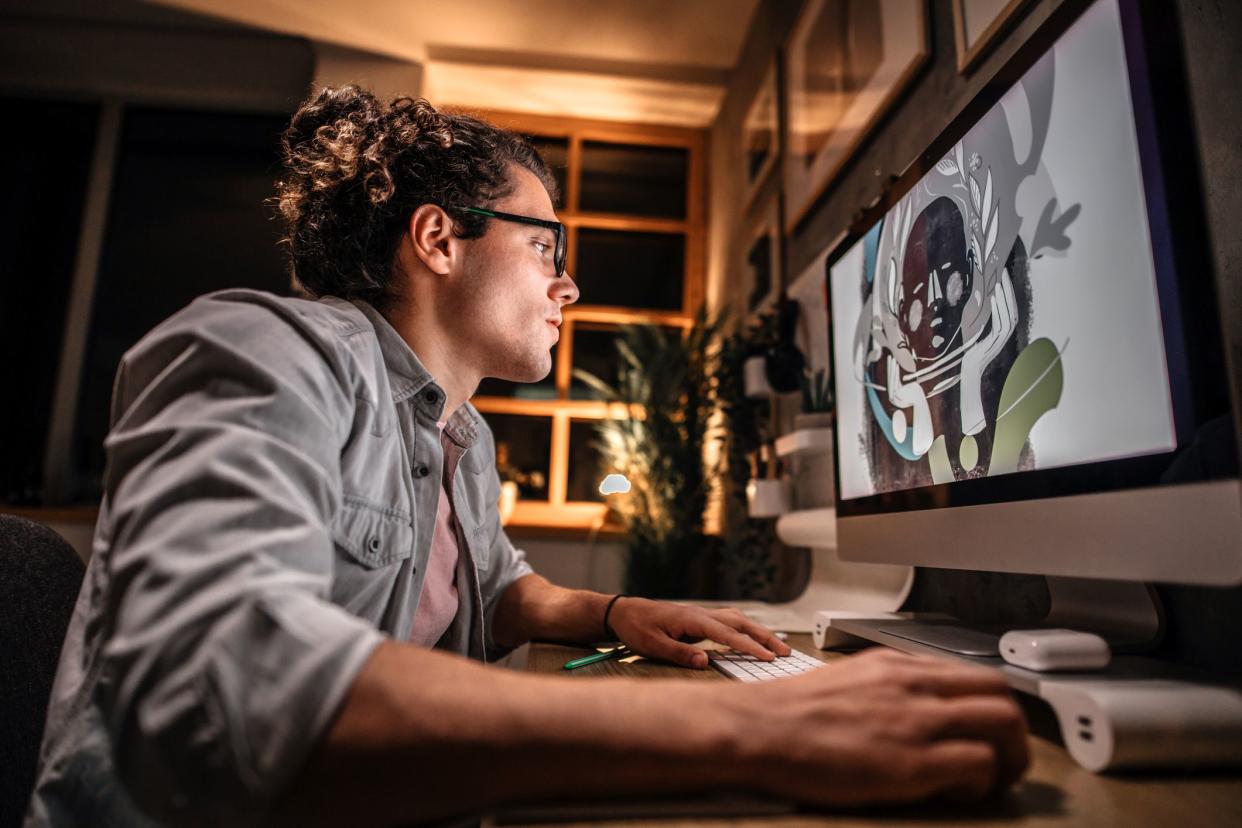 Young graphic designer working late night in his studio office. Sketching on paper and using computer for work.