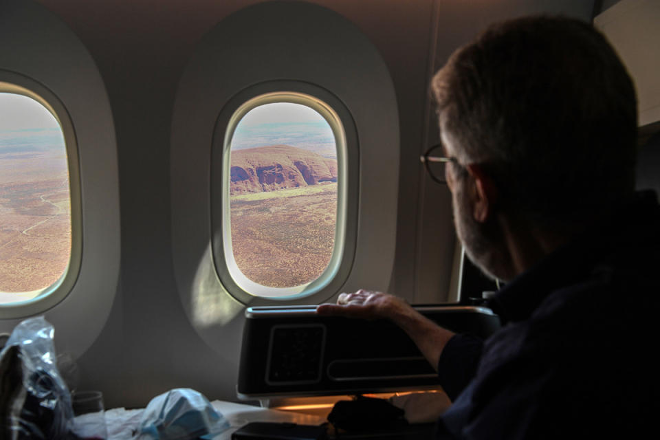 Male passenger looks at Uluru through window of Qantas aeroplane