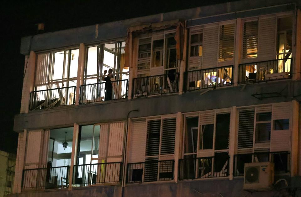 A person stands on the balcony of a building with a damaged facade