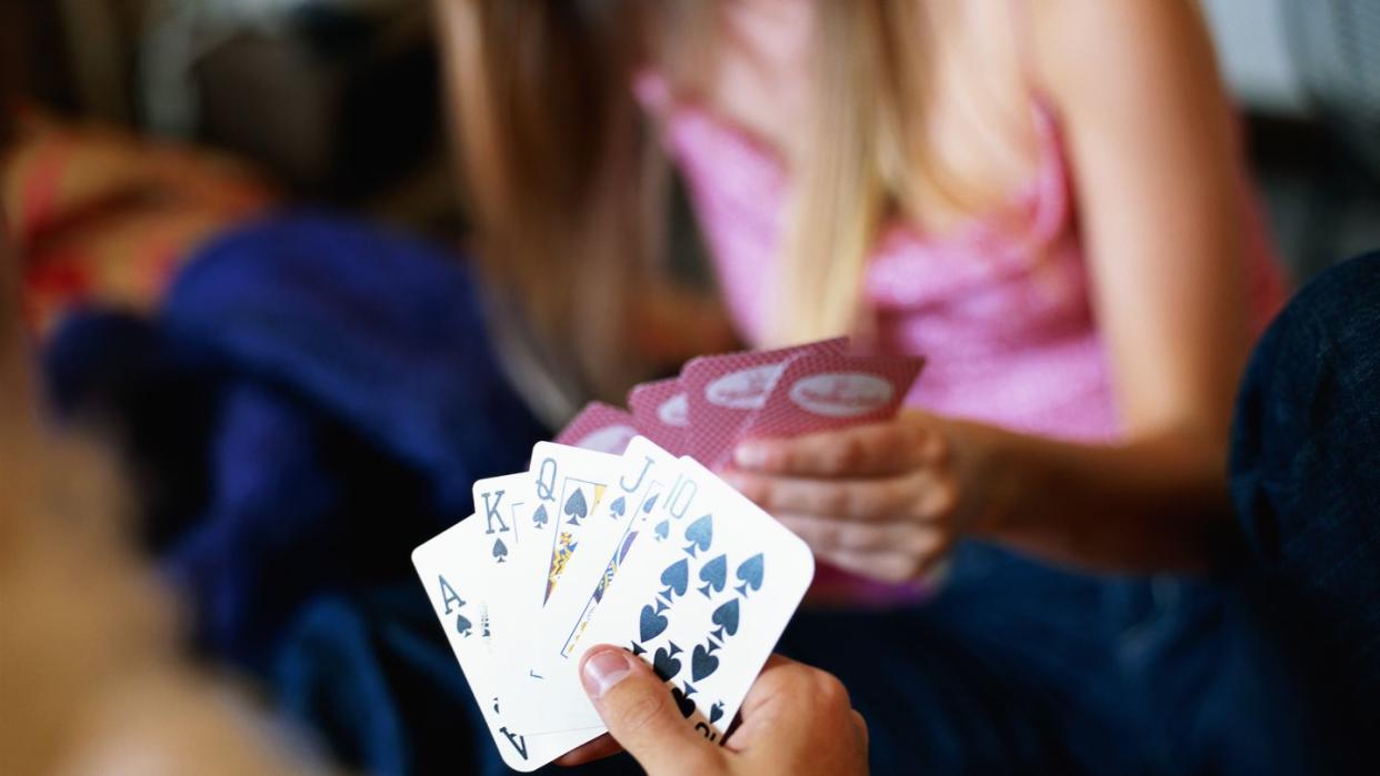 a man holding a stack of cards, focus on the cards, woman with cards is out of focus in front of him