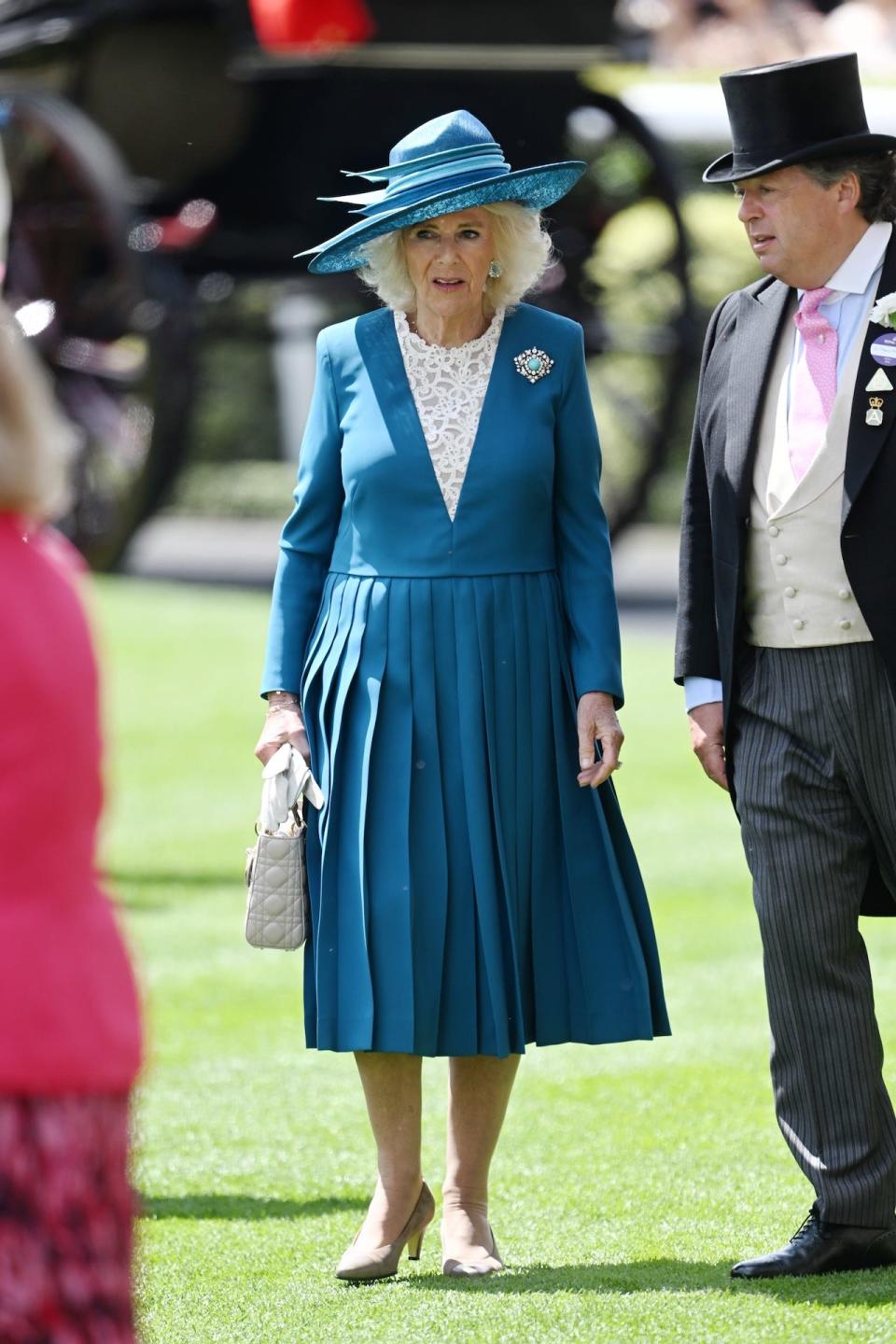 Queen Camilla wearing a pleated blue dress with white lace detailing.