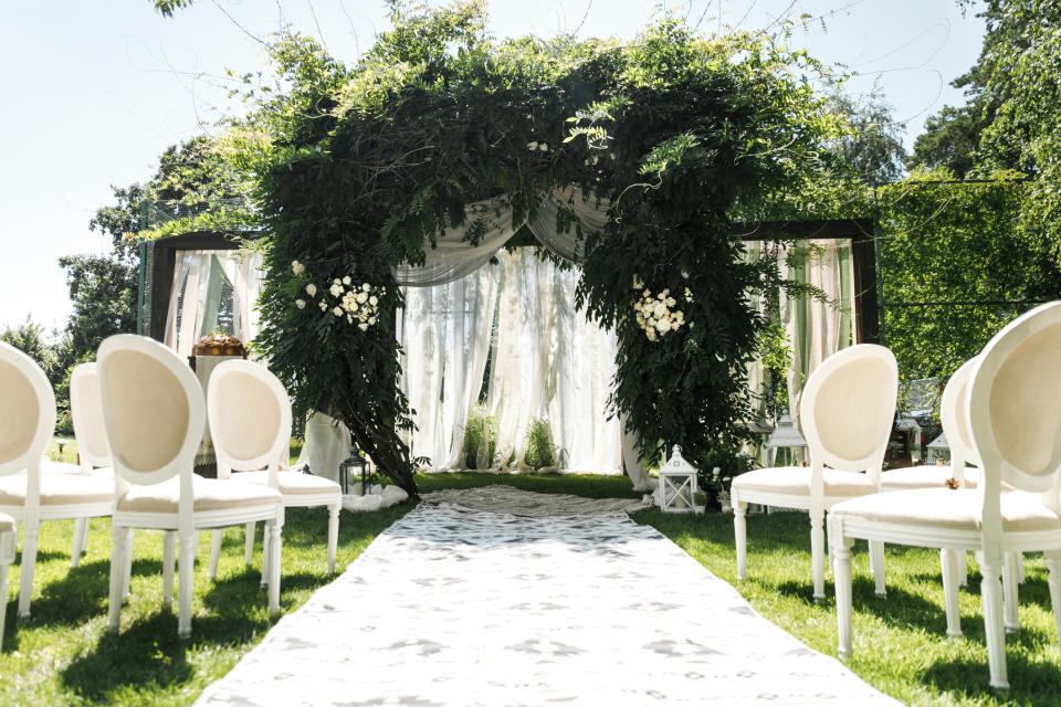 Outdoor wedding ceremony setup with white chairs arranged on either side of an aisle leading to an altar adorned with greenery and white flowers