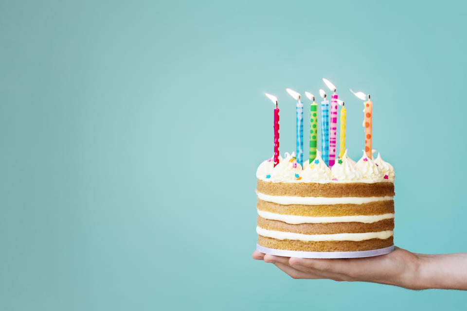 Hand holding a layered vanilla cake with colorful candles