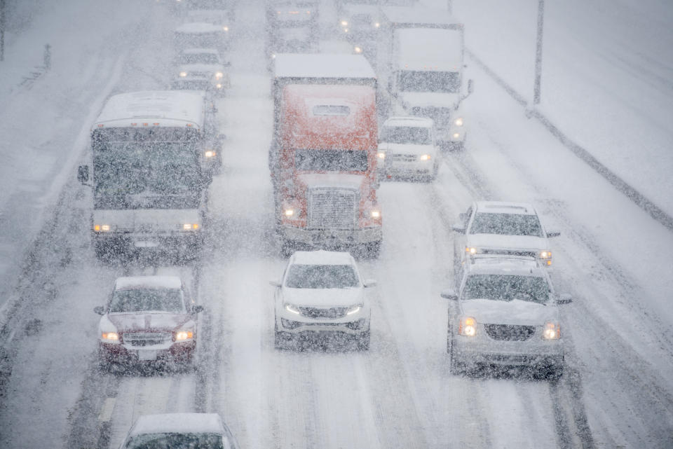 Several vehicles are traveling slowly down a multi lane road on an icy stormy day.