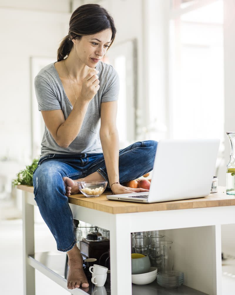 A woman sits on a kitchen counter with her laptop