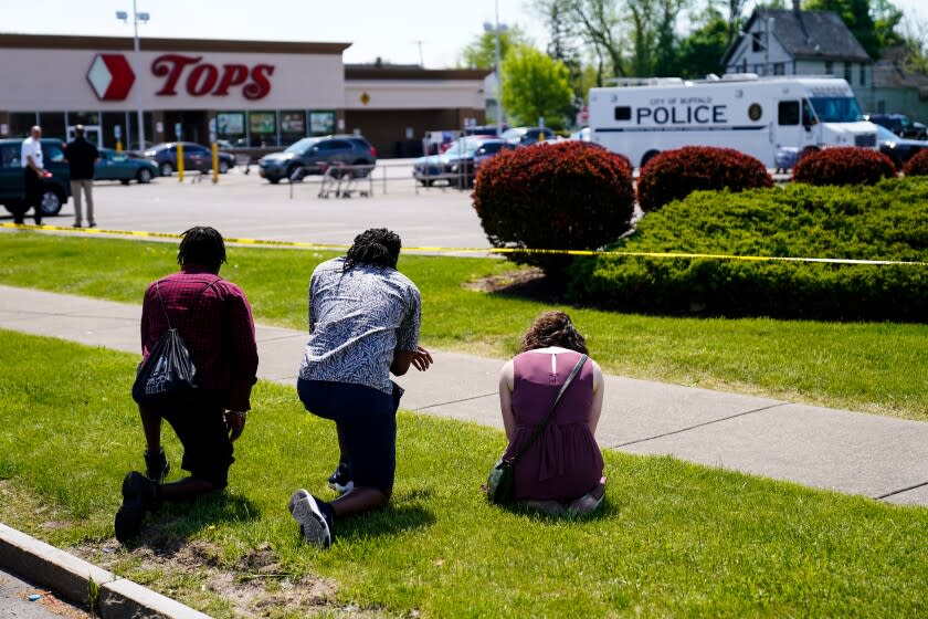 People pray outside the scene of a shooting at a supermarket, in Buffalo, N.Y., Sunday, May 15, 2022. A white 18-year-old wearing military gear and livestreaming with a helmet camera opened fire with a rifle at a supermarket in Buffalo, killing and wounding people in what authorities described as "racially motivated violent extremism." (AP Photo/Matt Rourke)