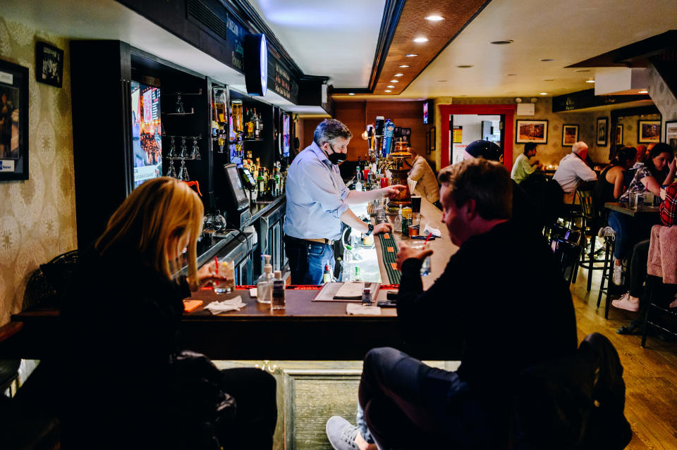 A bartender wearing a protective mask talks to customers sitting at the bar at Blooms Tavern in New York City in May. (Nina Westervelt/Bloomberg via Getty Images)