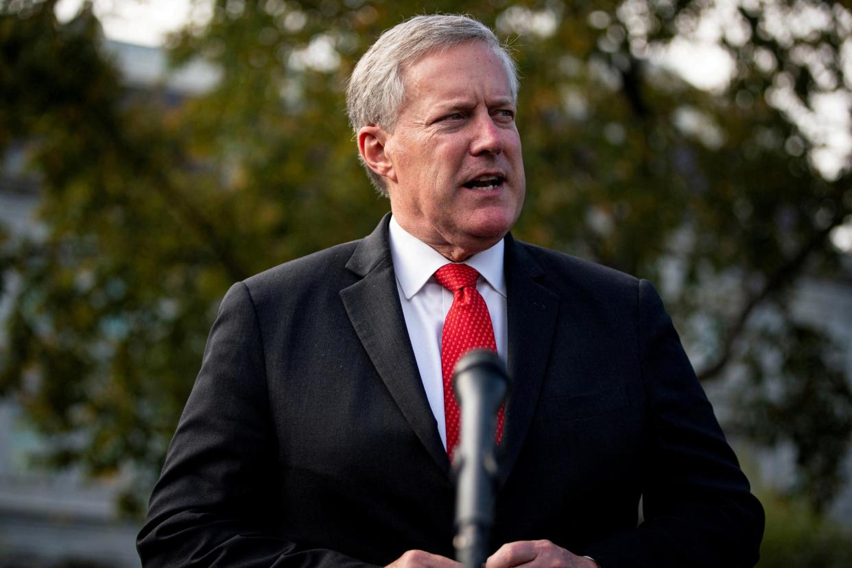 Meadows speaks in front of a microphone, wears a red tie.