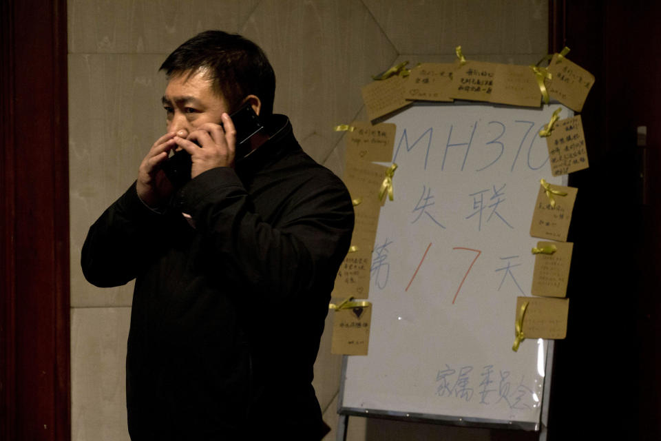 A man whispers on a cellphone near a board which reads "MH370 missing day 17" at a room reserved for relatives of Chinese passengers aboard the missing Malaysia Airlines jet in Beijing, China, Monday, March 24, 2014. Rain was expected to hamper the hunt Monday for debris suspected of being from the missing Malaysia Airlines jet, as the United States prepared to move a specialized device that can locate black boxes into the south Indian Ocean region. (AP Photo/Ng Han Guan)