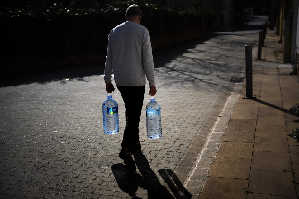 Joan Torrent, 64, walks toward his house carrying two plastic jugs of water refilled at a natural spring in Gualba, about 50 km, (31 miles) northwest of Barcelona, Spain, Wednesday, Jan 31, 2024. Joan trudges almost every day into the woods in search of drinking water. Spain's northeast Catalonia is preparing to declare a drought emergency for the area of some six million people including the city of Barcelona. But thousands of people who live in villages and towns in the Catalan countryside have already been in full-blown crisis mode for several months. (AP Photo/Emilio Morenatti)