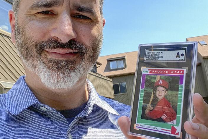This photo provided on Wednesday, Aug. 3, 2022, shows Allie Tarantino holding a baseball card featuring a very young Mark Zuckerberg grinning in a red jersey and gripping a bat. For 30 years Tarantino kept the baseball card filed it away in his basement, not knowing Zuckerberg would someday become a household name. (Shira Tarantino via AP)