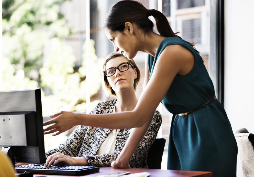 Businesswoman explaining something to female colleague over computer at desk in office. 