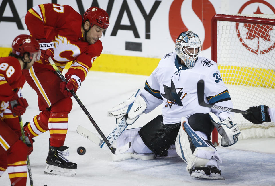 San Jose Sharks goalie Adin Hill, right, looks for the puck as Calgary Flames' Milan Lucic scrambles for the rebound during the second period of an NHL hockey game, Tuesday, Nov. 9, 2021 in Calgary, Alberta. (Jeff McIntosh/The Canadian Press via AP)