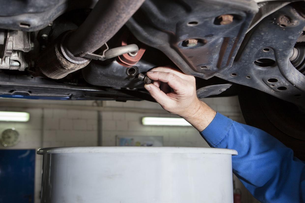 Auto repair shop - mechanic opens the oil drain plug of a modern car. Change of motor oil