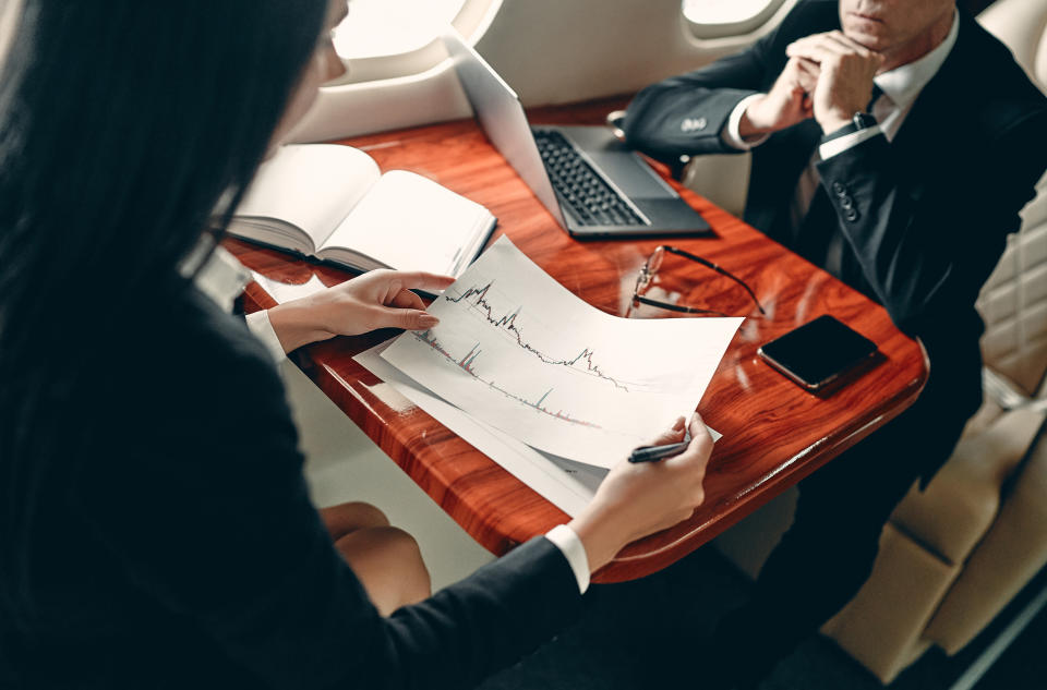 Business people in private jet. Young business woman and senior business man working while flying in aircraft. Successful work partners.