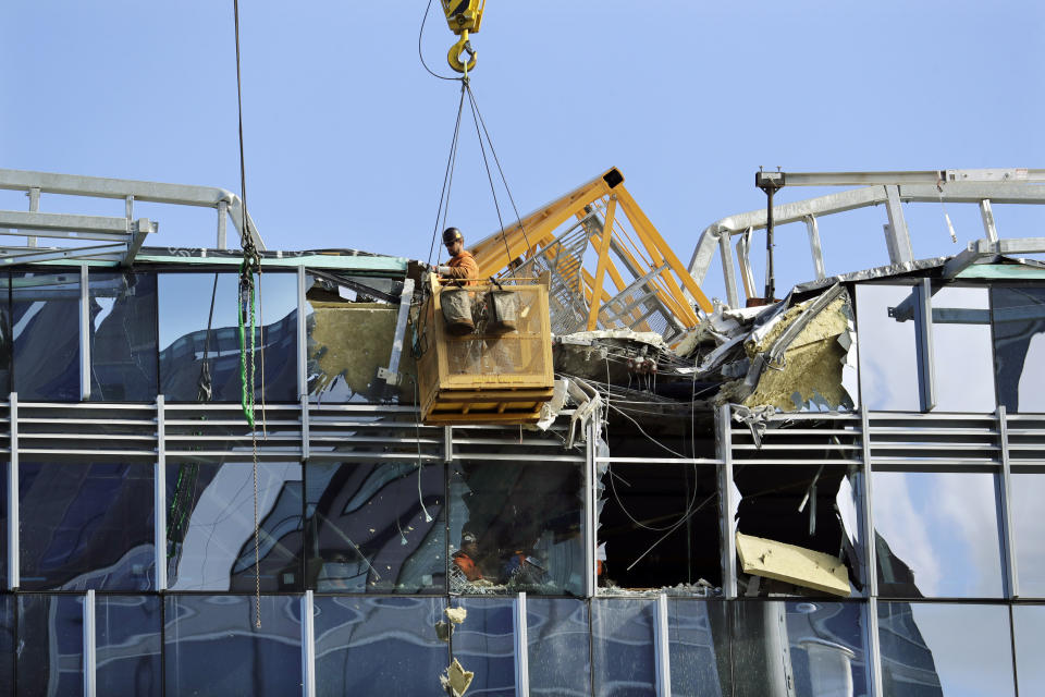 With a portion of the broken crane on the roof behind, a worker suspended in a basket clears debris from a building damaged when the crane atop it collapsed a day earlier, Sunday, April 28, 2019, in Seattle. The construction crane fell from a building on Google's new campus during a storm that brought wind gusts, crashing down onto one of the city's busiest streets and killing multiple people. (AP Photo/Elaine Thompson)