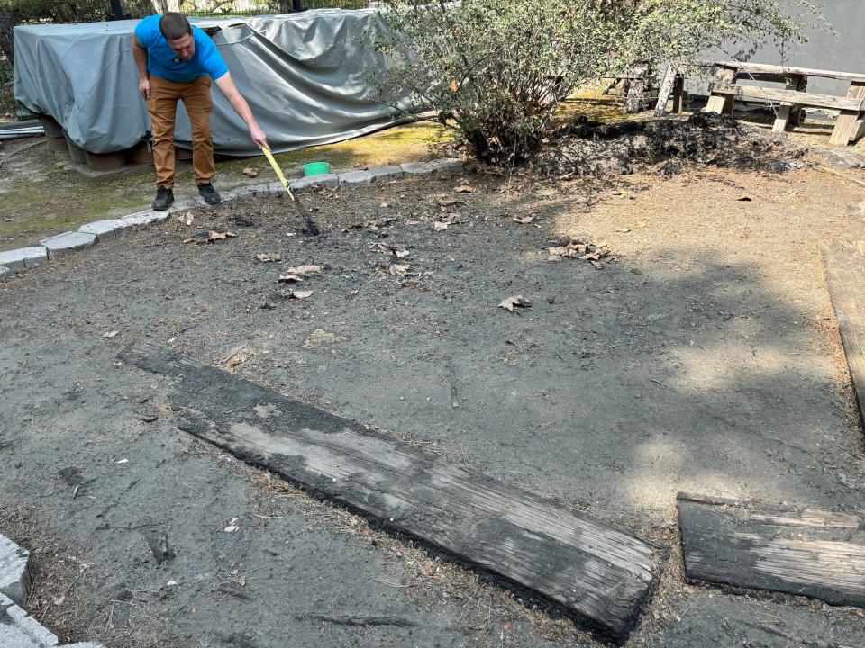 A person in a blue shirt and brown pants pulls a yellow stick stuck in a tar pit