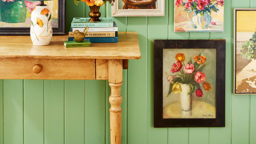 floral paintings of assorted size and frame style hung above and around a wood entry table on seafoam green wall