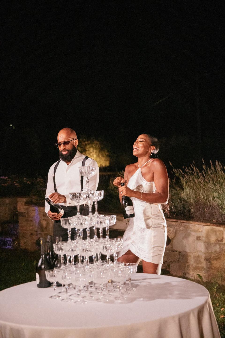 A bride and groom laugh as they pop champagne at their wedding.