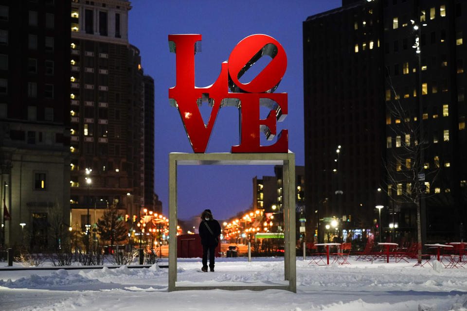 A person wearing a face mask as a precaution against the coronavirus walks during a winter storm near the Robert Indiana sculpture "LOVE" at John F. Kennedy Plaza, commonly known as Love Park, in Philadelphia, Monday, Feb. 1, 2021. (AP Photo/Matt Rourke)