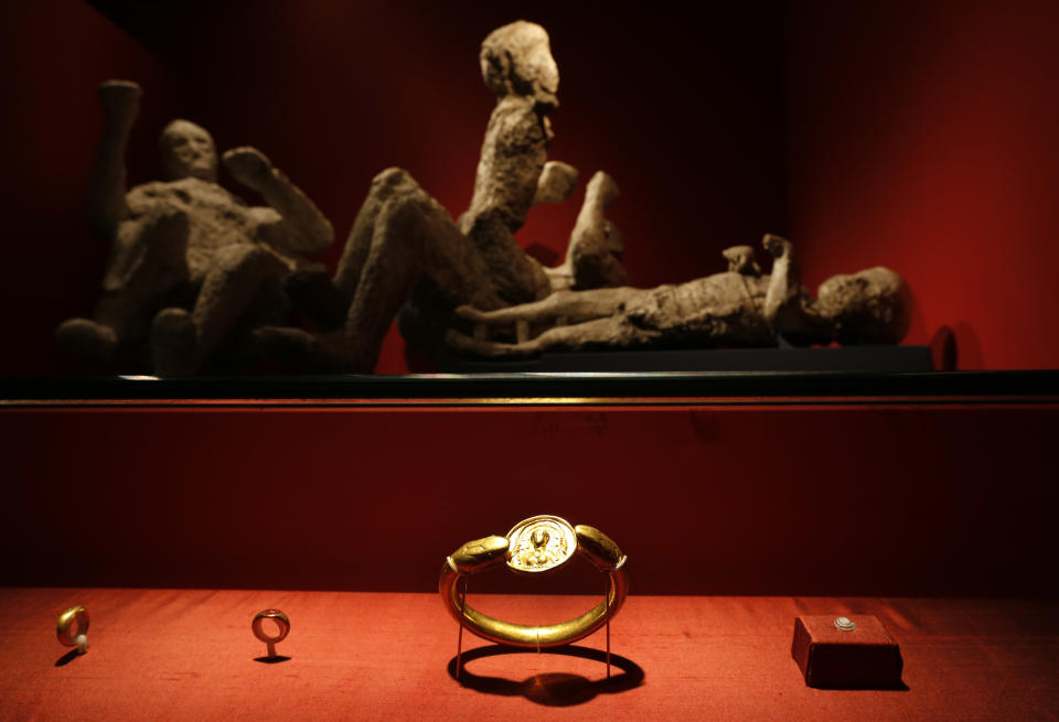 Jewellery found in the ruins of a house in Pompeii are displayed, backdropped by the casts of a family of two adults and two children who died together in the house in Pompeii, are seen during a photo call for the upcoming exhibition entitled 'Life and death Pompeii and Herculaneum', at the British Museum in central London, Tuesday, March 26, 2013. The casts were made by filling plaster in the void left by their bodies. The exhibition about the two Roman cities, buried by a catastrophic volcanic eruption of Mount Vezuvius in 79 AD, will run at the museum from March 28 to Sept. 29, 2013. (AP Photo/Lefteris Pitarakis)