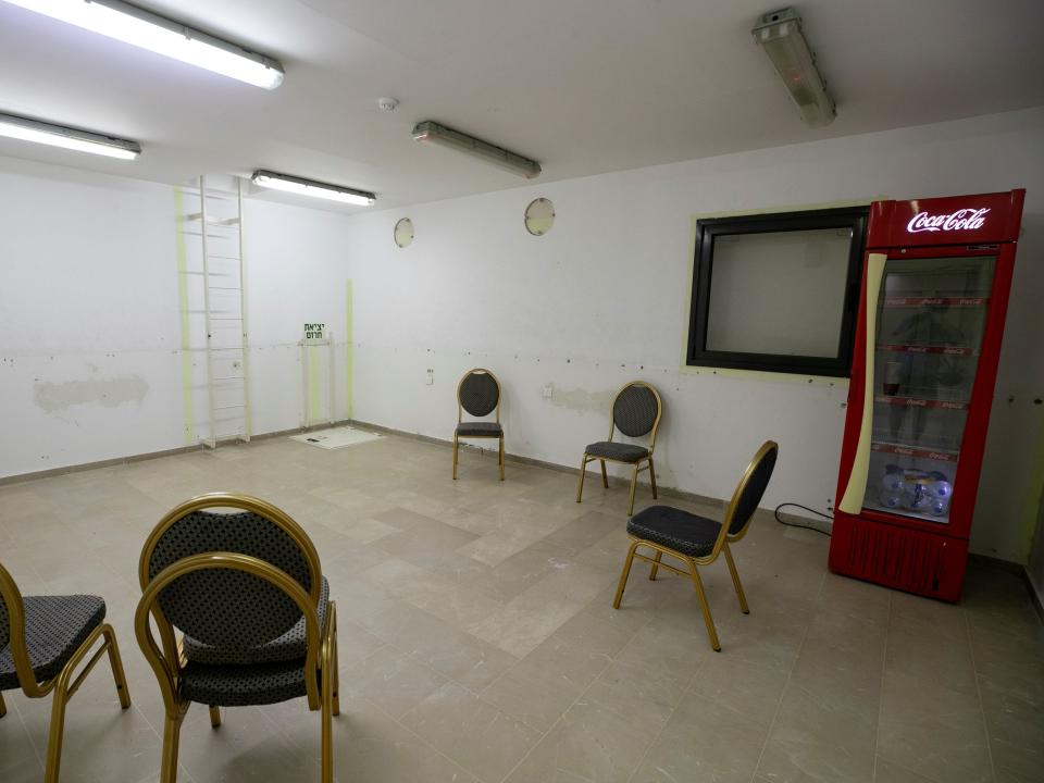 A safe room in a building in Jerusalem shows a vending machine and five chairs under fluorescent lights and bare white walls.