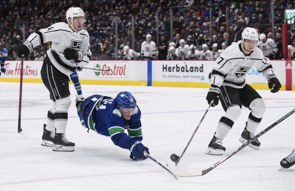 Vancouver Canucks' Bo Horvat (53) dives to reach the puck between Los Angeles Kings' Mikey Anderson, left, and Lias Andersson, of Sweden, during the second period of an NHL hockey action in Vancouver, British Columbia, Monday, Dec. 6, 2021. (Darryl Dyck/The Canadian Press via AP)