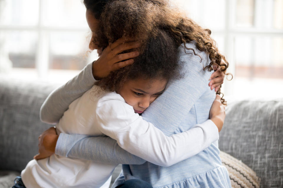 A child and their mother share a comforting hug on a couch, showcasing a tender moment of affection and support between them