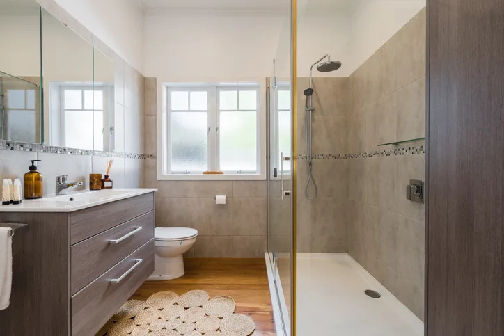 Modern bathroom with a walk-in shower, toilet, and vanity. There's a frosted window and tiled walls