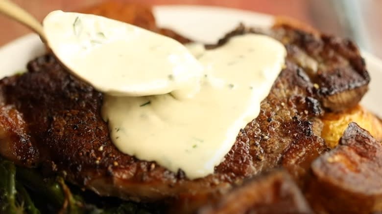 spooning blue cheese sauce on steak