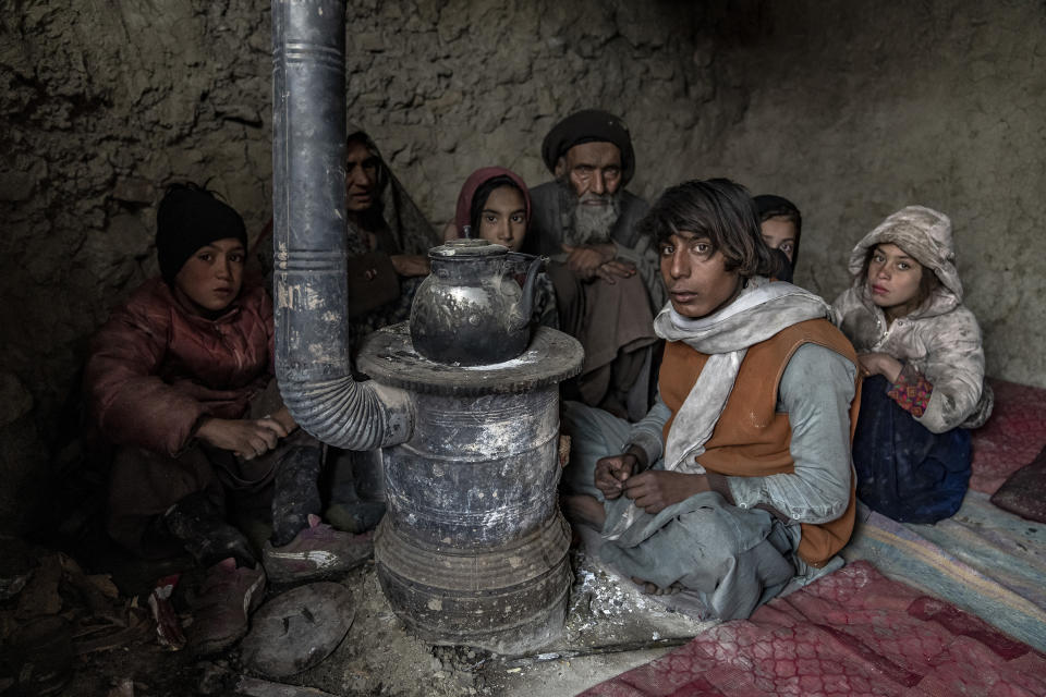 An internally displaced family huddle by a stove lit by burning garbage to keep warm in a camp on the outskirts of Kabul, Afghanistan, Sunday, Jan. 29, 2023. Over 3 million people are displaced within the country of 40 million, driven from their homes by war, earthquakes, drought or depleting resources. (AP Photo/Ebrahim Noroozi)