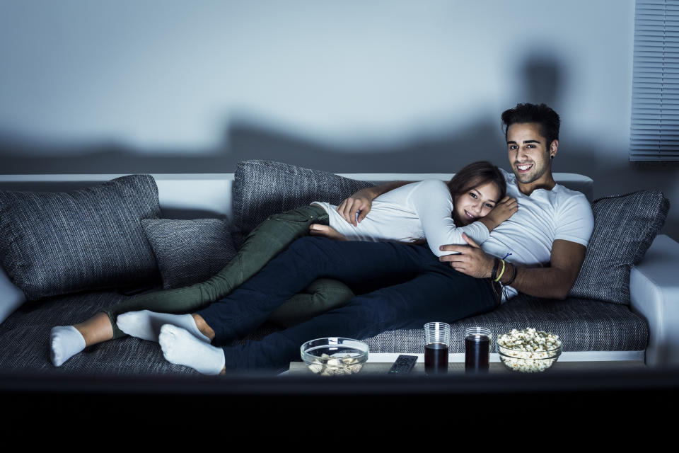 Young couple watching a movie at home, lying on sofa. Both Caucasian, casual, about 25 years old. (Photo: GoodLifeStudio via Getty Images)