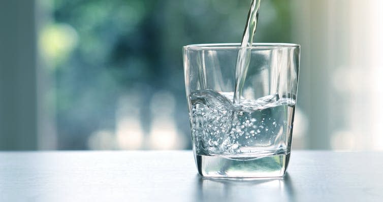 A glass on a table being filled with water.