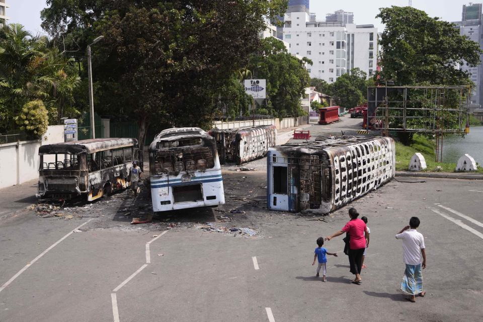 A Sri Lankan family watches the wreckage of buses burnt in clashes in Colombo, Sri Lanka, Wednesday, May 11, 2022. Sri Lanka's defense ministry ordered security forces on Tuesday to shoot anyone causing injury to people or property to contain widespread arson and mob violence targeting government supporters. (AP Photo/Eranga Jayawardena)