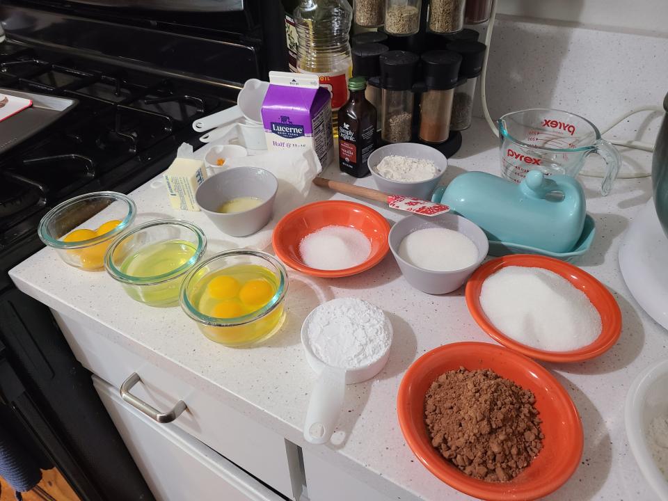 Bowls of flour and sugar and other baking ingredients are laid out on a busy countertop.