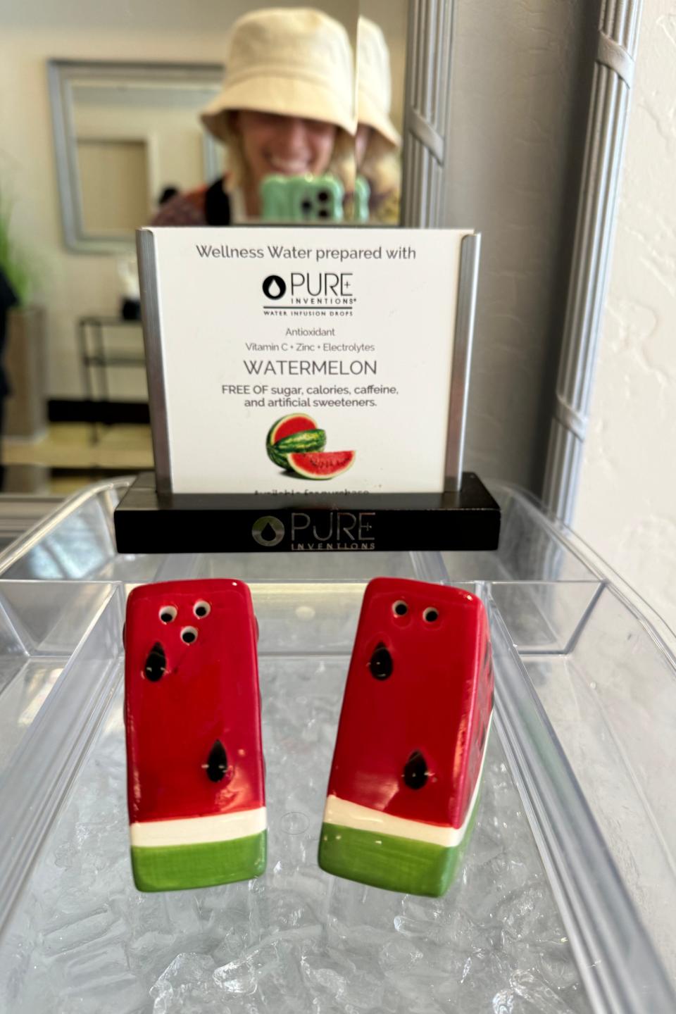 Smiling person behind counter offering watermelon-flavored hydration packets at a wellness water station