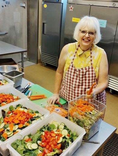 Community Kitchen volunteer Peggy Daniels not only makes a mean salad, but she does it in style! She is wearing one of the aprons that she made and donated to Community Kitchen. Peggy hunts for old, cotton tablecloths at garage sales and thrift stores and then turns them into aprons. Community volunteers like Peggy are needed now to "fill the volunteer gap" at organizations around town while students and regular volunteers are on vacation.